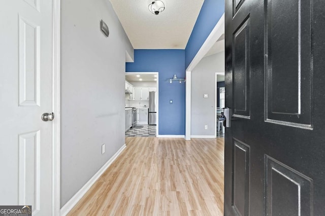 foyer entrance featuring light wood finished floors, baseboards, and a textured ceiling