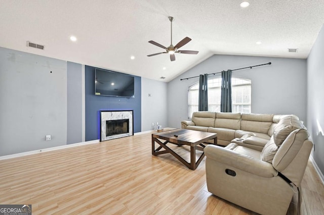 living room with a fireplace, lofted ceiling, visible vents, light wood-style flooring, and a textured ceiling