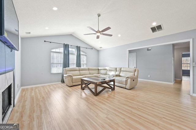 living area with light wood-style floors, visible vents, vaulted ceiling, and a tile fireplace