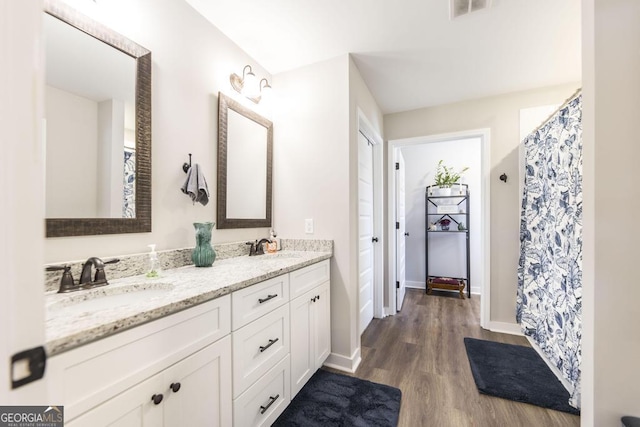 full bathroom featuring double vanity, visible vents, a sink, and wood finished floors