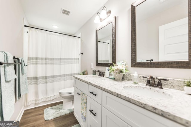 bathroom featuring toilet, visible vents, a sink, and wood finished floors