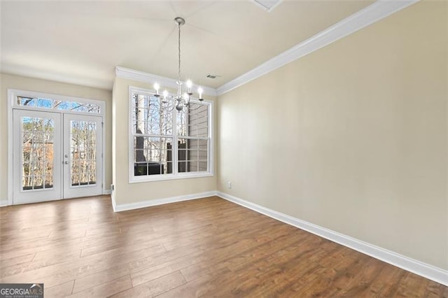 unfurnished dining area featuring french doors, an inviting chandelier, ornamental molding, wood finished floors, and baseboards