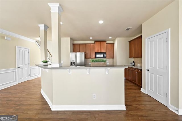 kitchen featuring black microwave, a breakfast bar area, brown cabinetry, stainless steel fridge with ice dispenser, and an island with sink