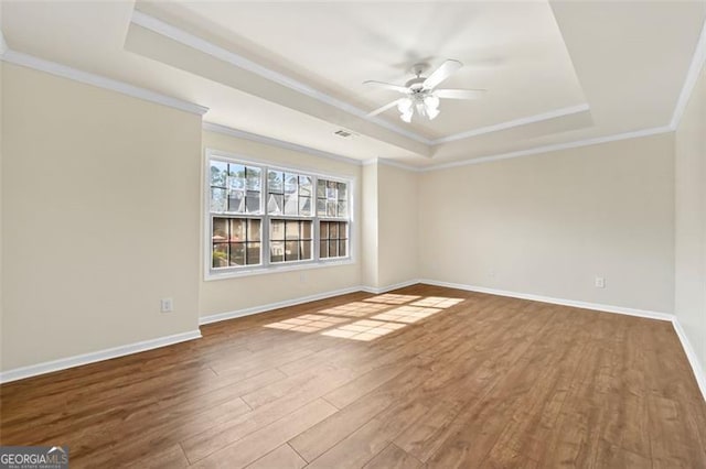 unfurnished room with ceiling fan, wood finished floors, baseboards, a raised ceiling, and crown molding