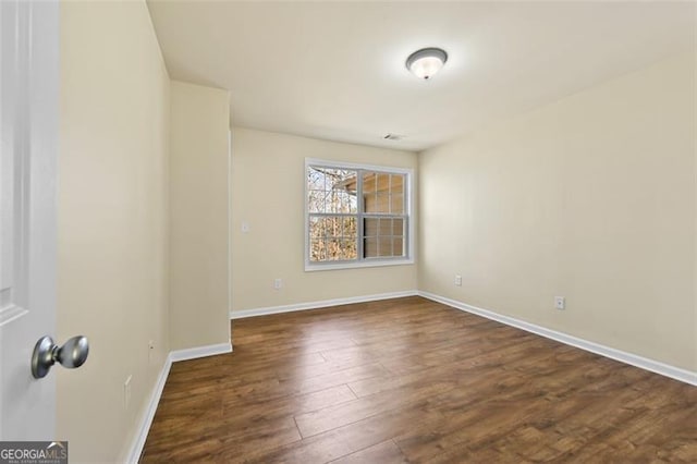 empty room featuring dark wood-type flooring, visible vents, and baseboards