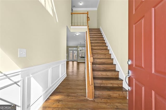 stairway featuring a wainscoted wall, ornamental molding, wood finished floors, and a decorative wall