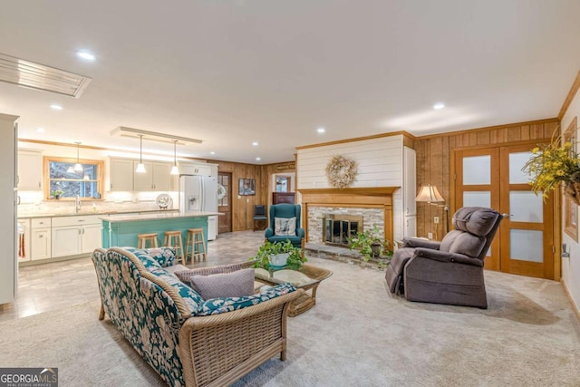 living area featuring french doors, a fireplace, recessed lighting, ornamental molding, and wooden walls