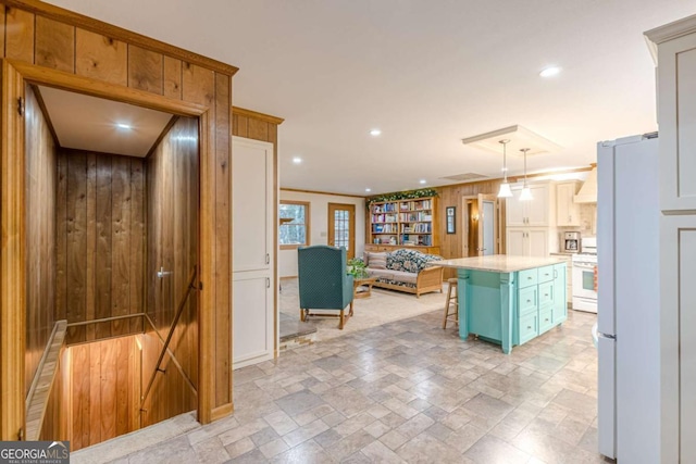 kitchen with pendant lighting, light countertops, a kitchen island, wood walls, and white appliances