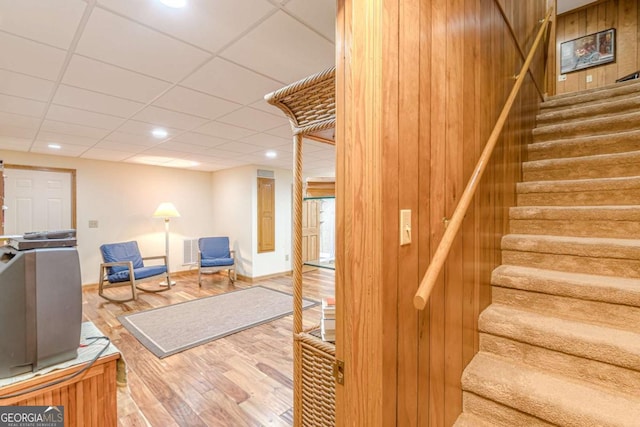 staircase with a paneled ceiling, wood walls, visible vents, and wood finished floors