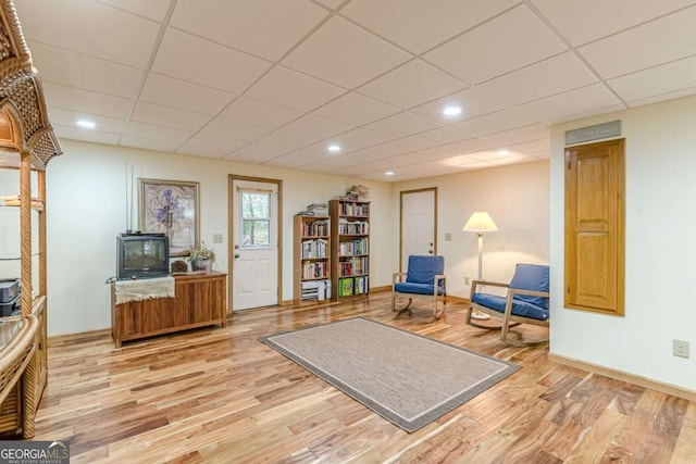 living area featuring baseboards, a drop ceiling, and light wood finished floors