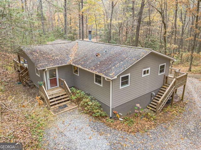 view of front of house featuring gravel driveway, a shingled roof, and stairway