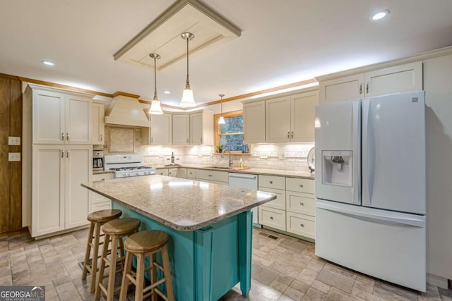 kitchen featuring white appliances, tasteful backsplash, a kitchen island, decorative light fixtures, and light stone countertops