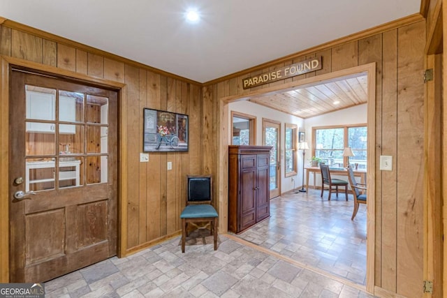 entryway featuring lofted ceiling, wooden walls, stone finish floor, and ornamental molding