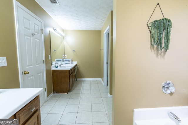 full bath with a textured ceiling, a bathing tub, vanity, baseboards, and tile patterned floors