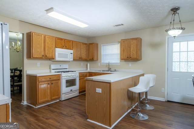 kitchen featuring white appliances, dark wood-style flooring, a breakfast bar, a sink, and visible vents