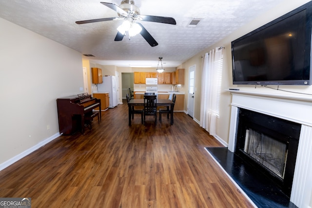 living area featuring dark wood finished floors, a fireplace with raised hearth, visible vents, a textured ceiling, and baseboards