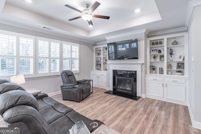 living area featuring light wood-style floors, a tray ceiling, and a glass covered fireplace