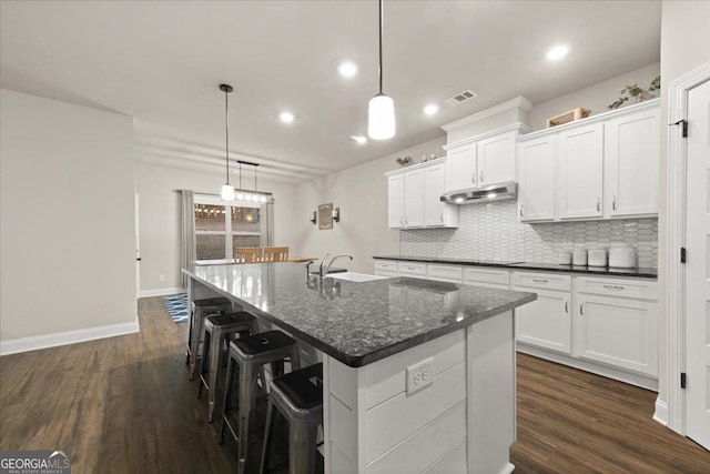 kitchen featuring backsplash, dark wood finished floors, visible vents, and under cabinet range hood