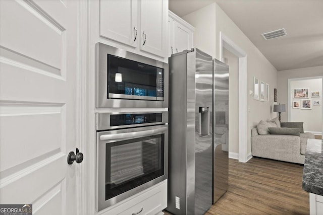 kitchen with visible vents, dark wood finished floors, appliances with stainless steel finishes, dark stone countertops, and white cabinetry