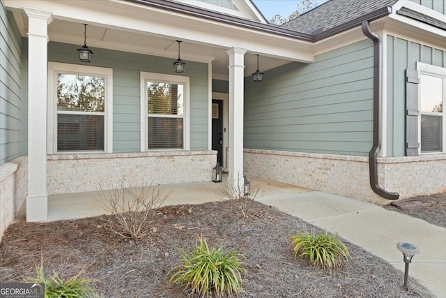 view of exterior entry featuring covered porch, a shingled roof, and board and batten siding