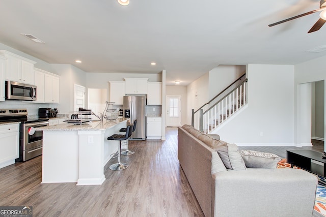 kitchen with stainless steel appliances, visible vents, open floor plan, a kitchen island with sink, and white cabinetry
