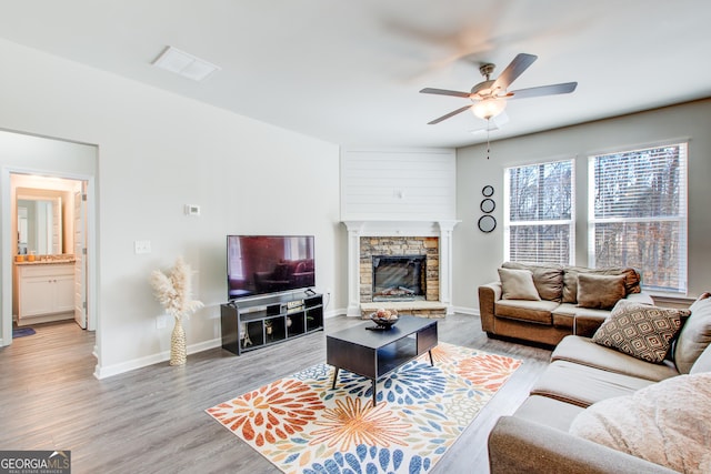 living room with light wood-type flooring, a fireplace, a ceiling fan, and baseboards