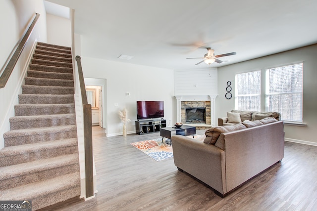living room with stairs, a fireplace, a ceiling fan, and wood finished floors