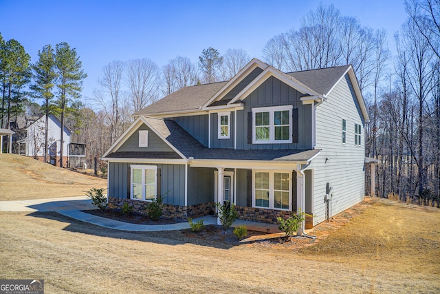 craftsman-style home with stone siding, a porch, board and batten siding, and a shingled roof