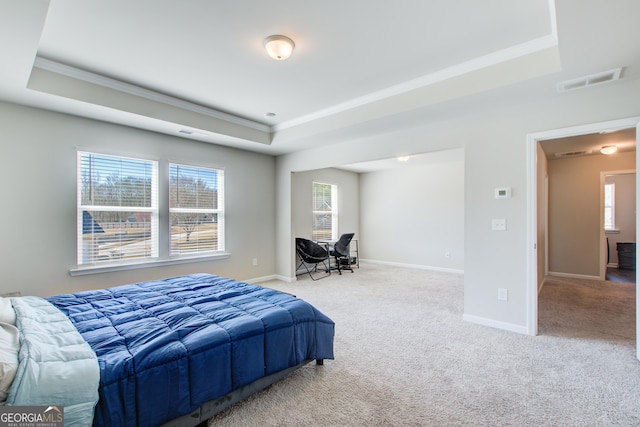 bedroom featuring light colored carpet, a tray ceiling, visible vents, and multiple windows