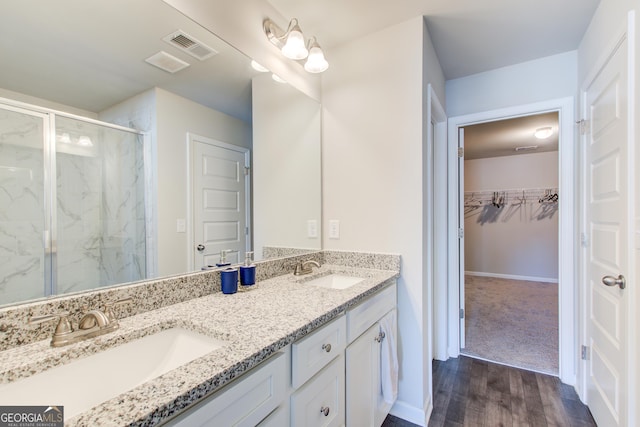 full bath featuring a sink, visible vents, a walk in closet, and a marble finish shower