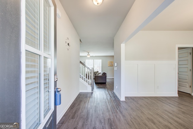 entryway with a decorative wall, stairway, wainscoting, ceiling fan, and wood finished floors