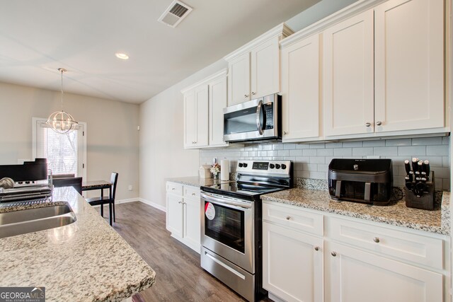 kitchen with pendant lighting, stainless steel appliances, visible vents, white cabinets, and a sink