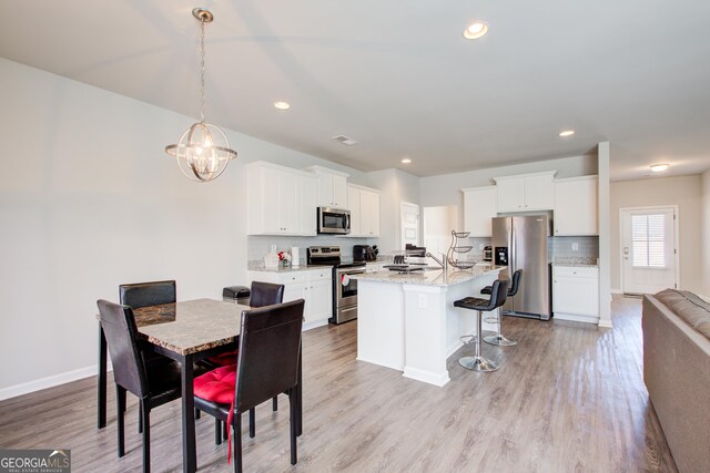 kitchen featuring appliances with stainless steel finishes, light stone countertops, light wood-type flooring, white cabinetry, and pendant lighting