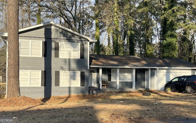 split level home featuring a porch, brick siding, and a garage