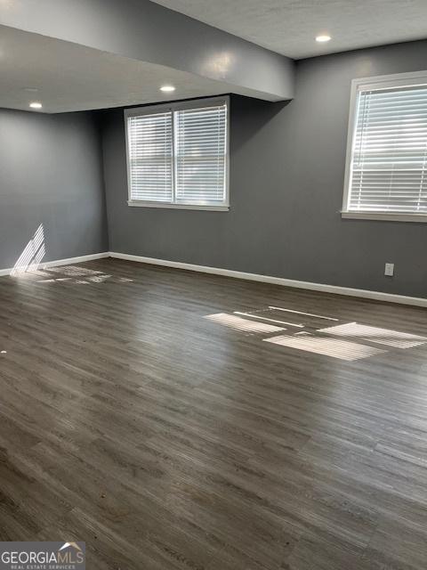 spare room featuring a healthy amount of sunlight, recessed lighting, dark wood finished floors, and baseboards