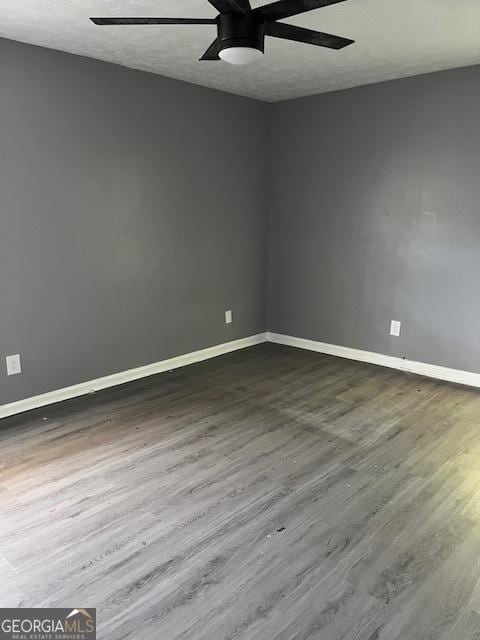 empty room with dark wood-style floors, ceiling fan, and baseboards
