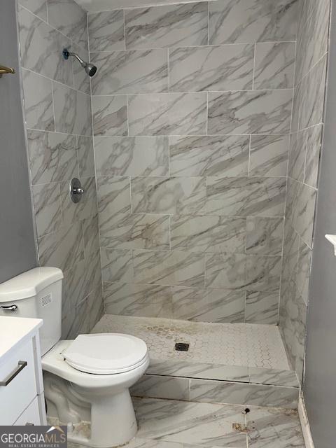 bathroom with toilet, a tile shower, marble finish floor, and vanity