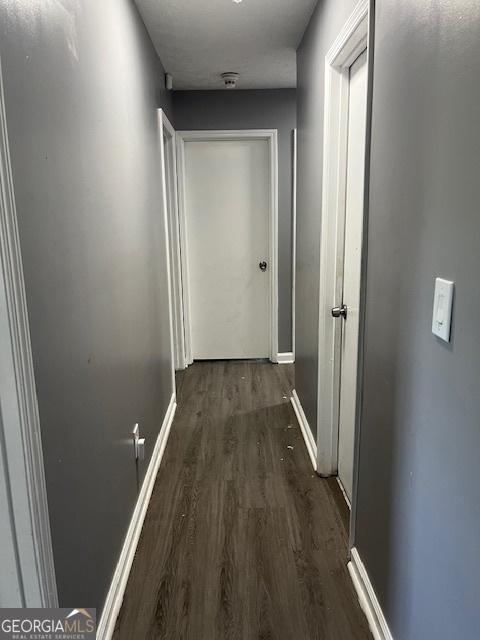 corridor with baseboards and dark wood-type flooring