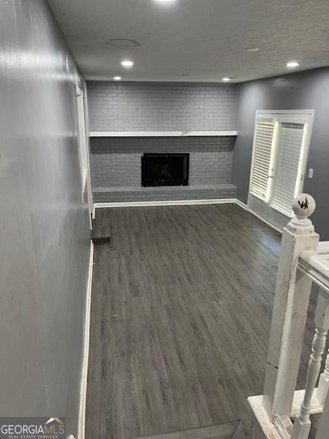 unfurnished living room featuring recessed lighting, wood finished floors, and a brick fireplace