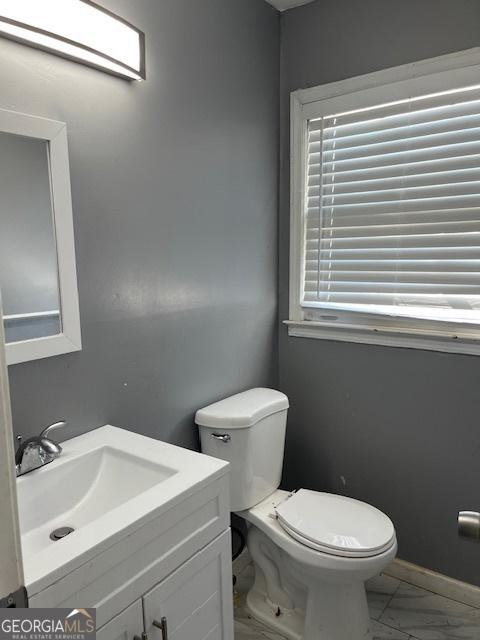 half bathroom featuring vanity, toilet, marble finish floor, and baseboards