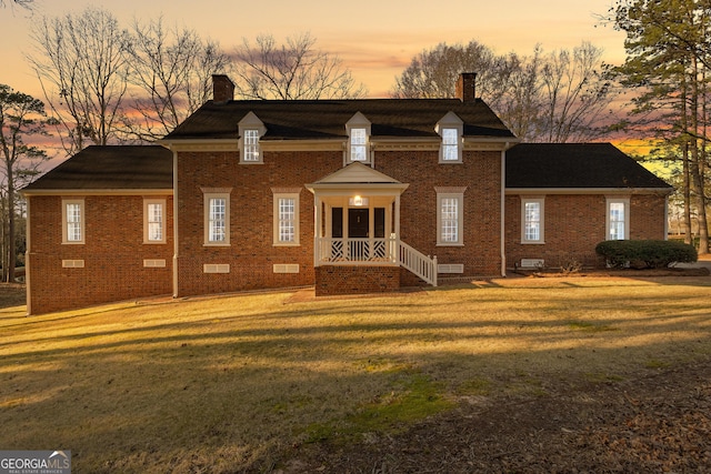 view of front of property featuring crawl space, brick siding, a yard, and a chimney