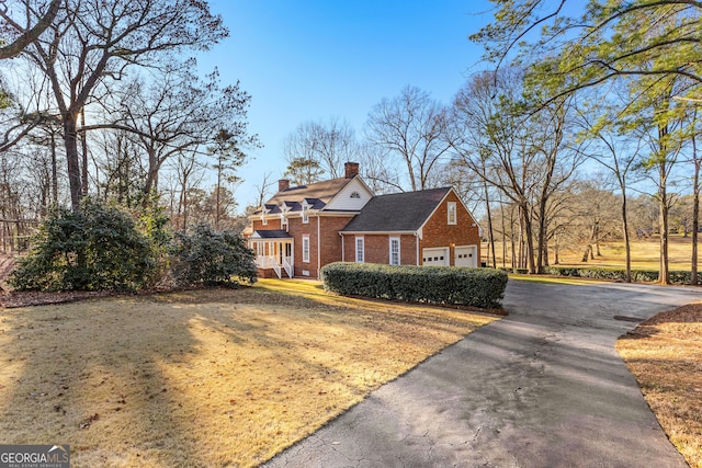 view of front facade with a garage, brick siding, driveway, and a chimney