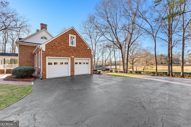 view of property exterior featuring a garage, brick siding, a chimney, and aphalt driveway