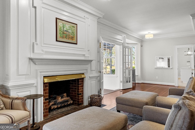 living area with ornamental molding, a brick fireplace, dark wood finished floors, and baseboards
