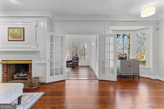 interior space featuring visible vents, ornamental molding, dark wood-style flooring, french doors, and a brick fireplace