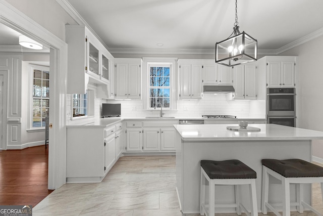 kitchen featuring stainless steel appliances, light countertops, glass insert cabinets, white cabinets, and under cabinet range hood