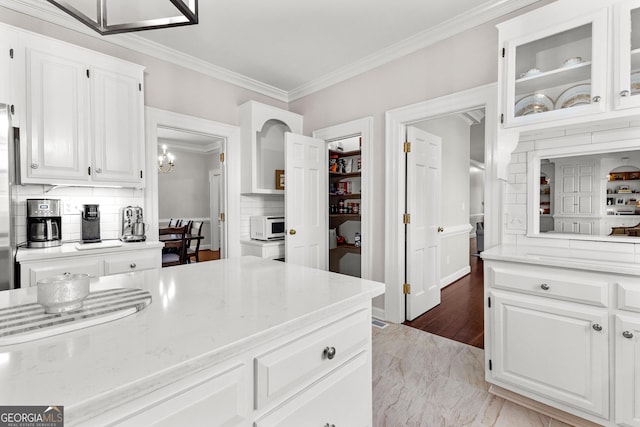 kitchen featuring glass insert cabinets, white microwave, white cabinetry, and crown molding