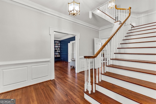 stairs with a wainscoted wall, crown molding, a decorative wall, wood finished floors, and a chandelier