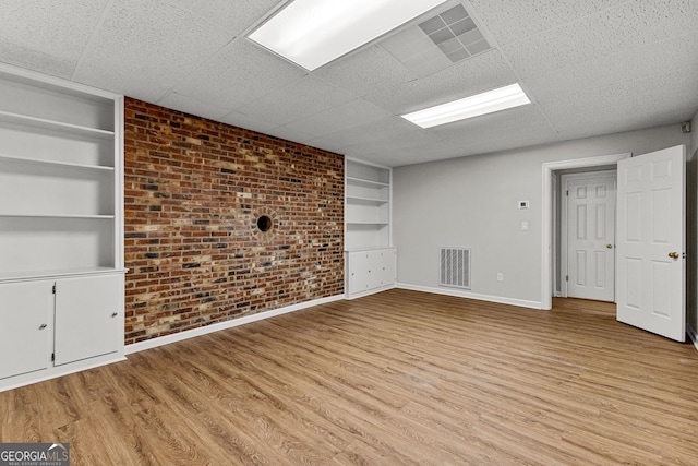unfurnished room with brick wall, visible vents, baseboards, built in features, and light wood-type flooring