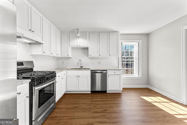 kitchen featuring white cabinets, appliances with stainless steel finishes, light stone countertops, under cabinet range hood, and a sink